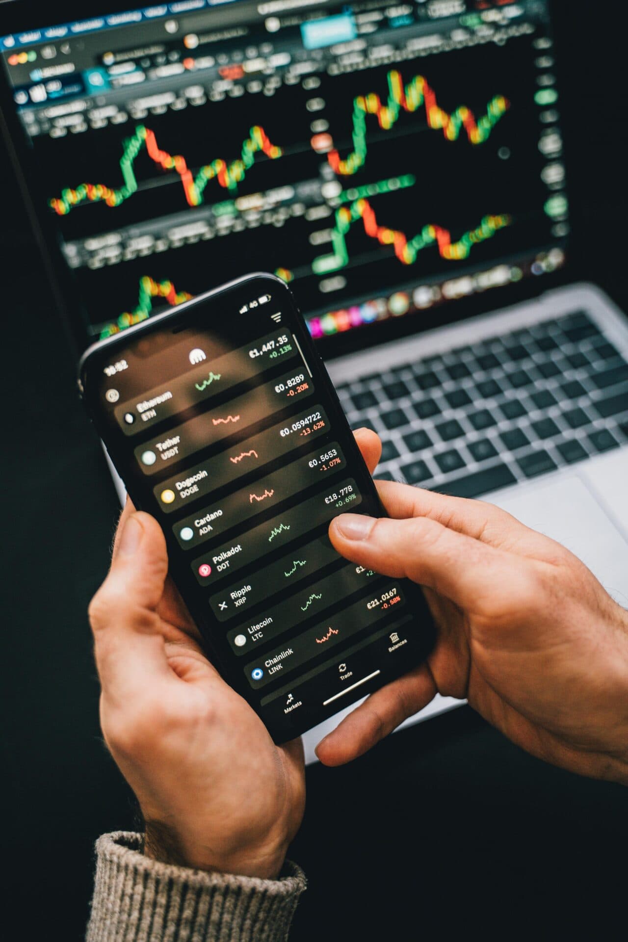 Phone showing a list of cryptocurrency prices in front of trading charts