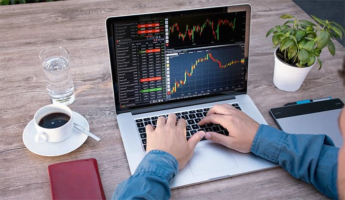 Trader's hands on a laptop showing candlestick charts